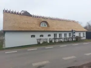 Gavl med mørk træbeklædning, hvor to tagflader med forskellig højde mødes i én sammenhængende rygning på Lotusgården